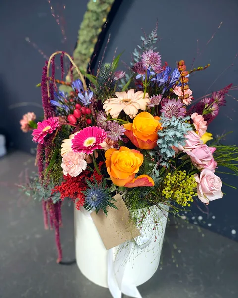 Flower box w jesiennych kolorach: Kompozycja w białym pudełku w ciepłych jesiennych barwach: pomarańczowe róże, różowe gerbery, pudrowe goździki i róże, niebieskie agapanty i mikołajki, uzupełnione czerwonymi jagodami, zwisającym amarantusem i srebrzystą zielenią. Kwiaciarnia Bukieteria Gorzów Wielkopolski