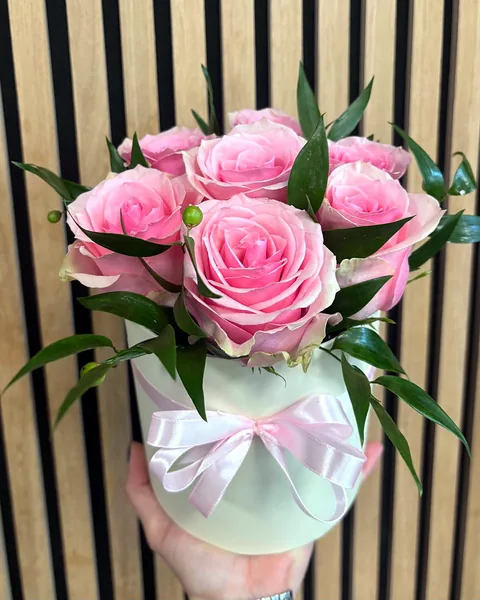 Flower box z różowymi różami: Okrągłe pudełko w kolorze ecru z kokardą, wypełnione różowymi różami i ciemnozieloną ruscusem. Kwiaciarnia Bukieteria Gorzów Wielkopolski