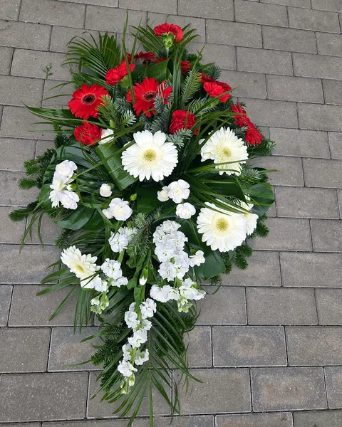 Wiązanka pogrzebowa biało-czerwona: Wiązanka pogrzebowa w biało-czerwonych barwach z gerberami, goździkami i maciejką, ułożona na świerku z palmą i liśćmi. Kwiaciarnia Bukieteria Gorzów Wielkopolski