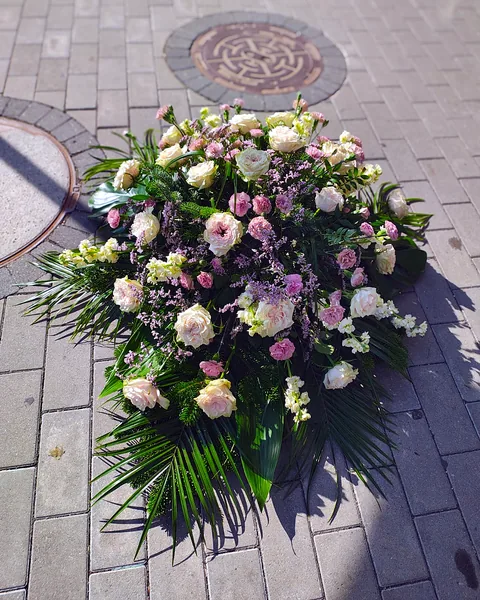 Wiązanka pogrzebowa w jasnych kolorach: Podłużna wiązanka na świerku z kremowymi różami, różowymi goździkami, białymi lewkoniami i liliowym limonium, wykończona liśćmi palmy i gałązkami jodły. Kwiaciarnia Bukieteria Gorzów Wielkopolski
